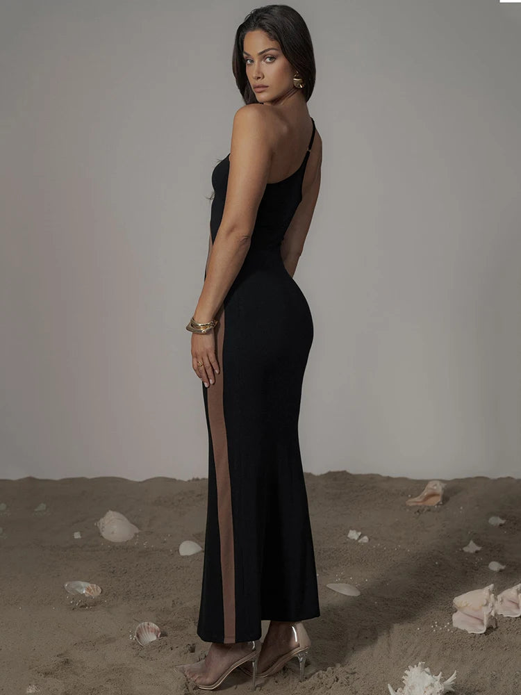 Woman wearing a black dress with a slit, standing on sandy ground.