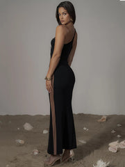 Woman wearing a black dress with a slit, standing on sandy ground.
