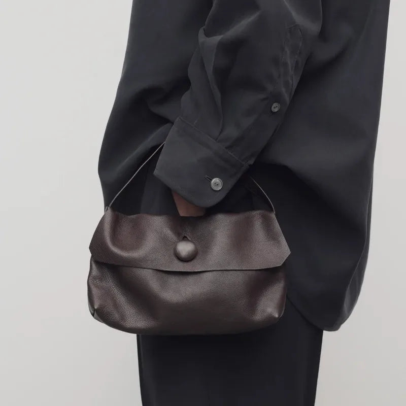 Person holding a brown leather bag against a plain background