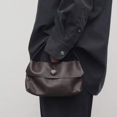 Person holding a brown leather bag against a plain background