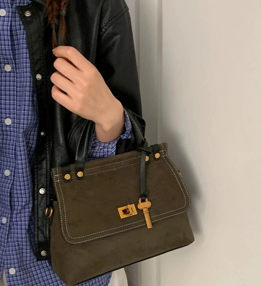 Person holding a brown leather handbag with a plain background