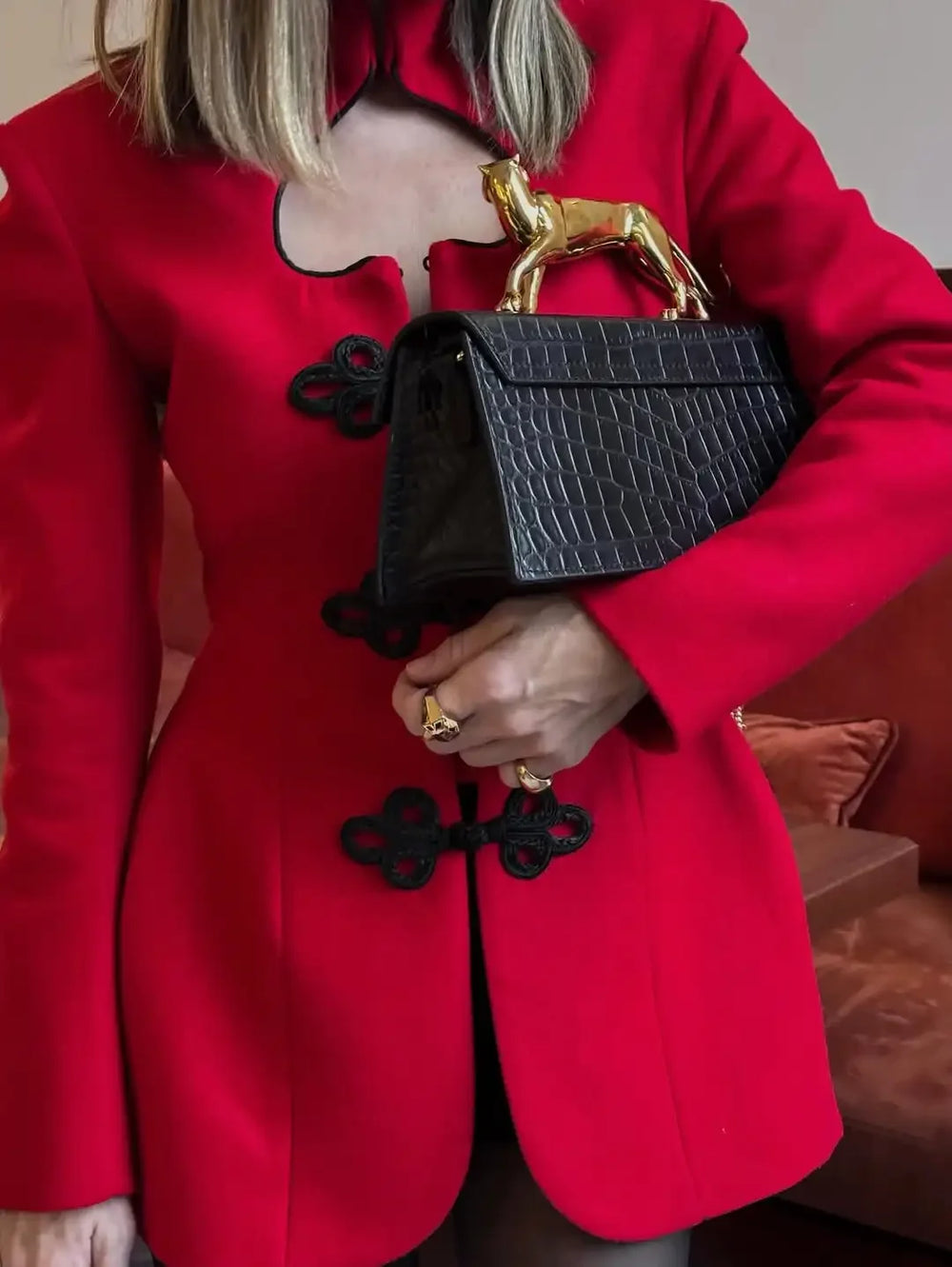 Person wearing a red coat holding a black handbag with a gold handle.