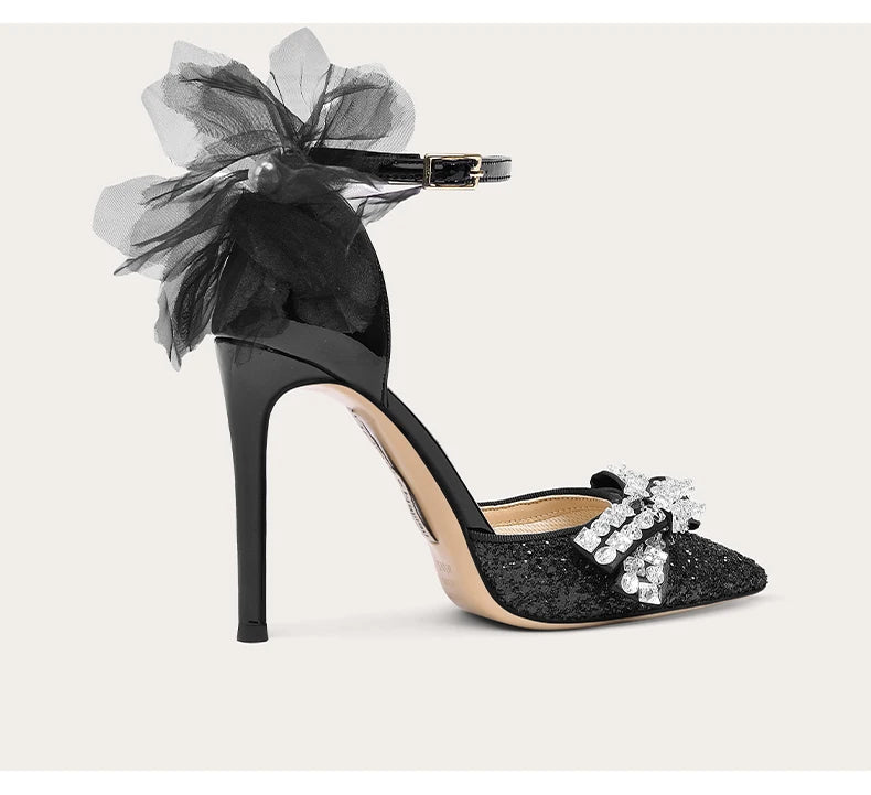 Black high-heeled shoe with decorative bow and embellishments on a light background