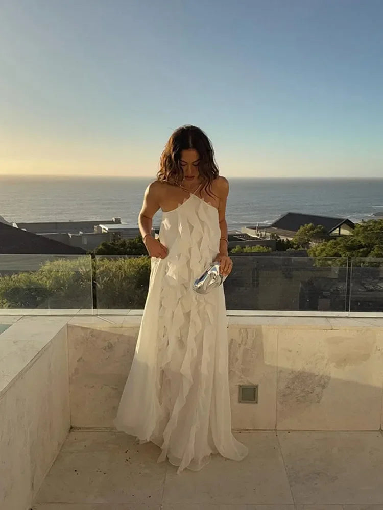 Woman in a white dress standing on a balcony with a scenic ocean view.