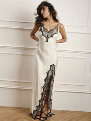 Woman wearing a white evening gown with black lace details against a white wall.