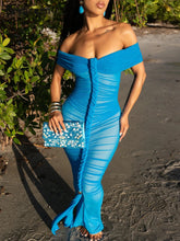 Woman wearing a blue off-shoulder dress with a mermaid tail design on a beach.