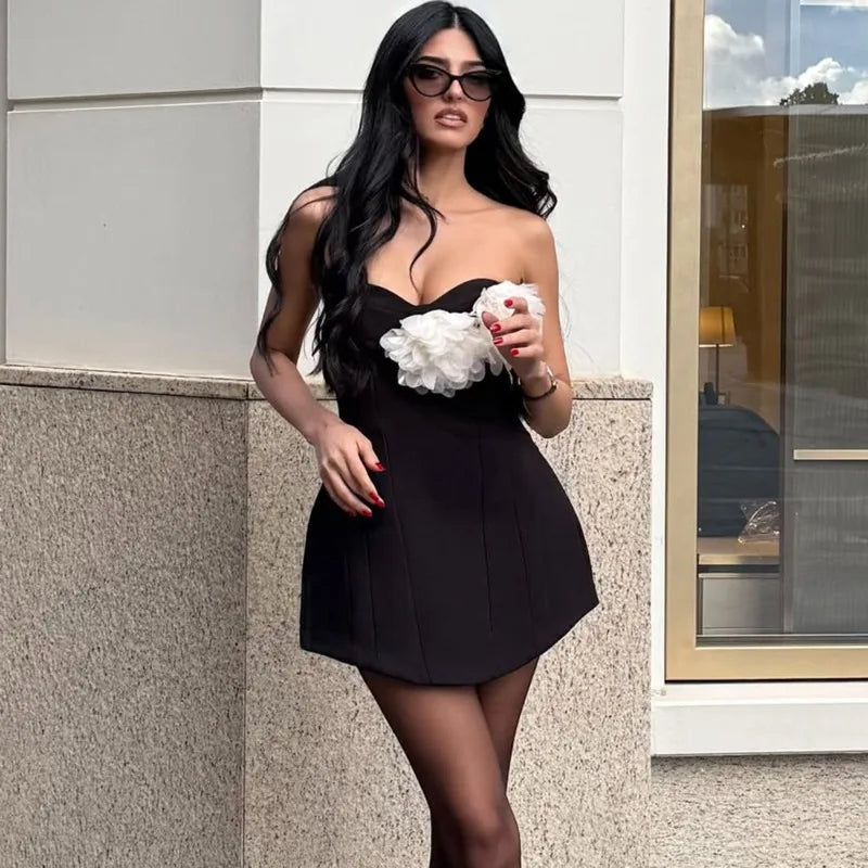 Woman in a black dress holding white flowers against a building exterior.