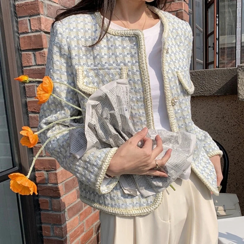 Person wearing a patterned jacket holding orange flowers against a brick wall.