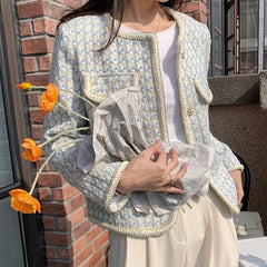 Person wearing a patterned jacket holding orange flowers against a brick wall.