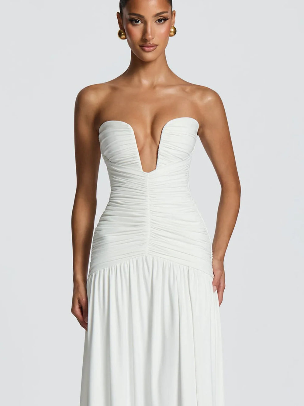 Woman wearing a strapless white gown against a plain background