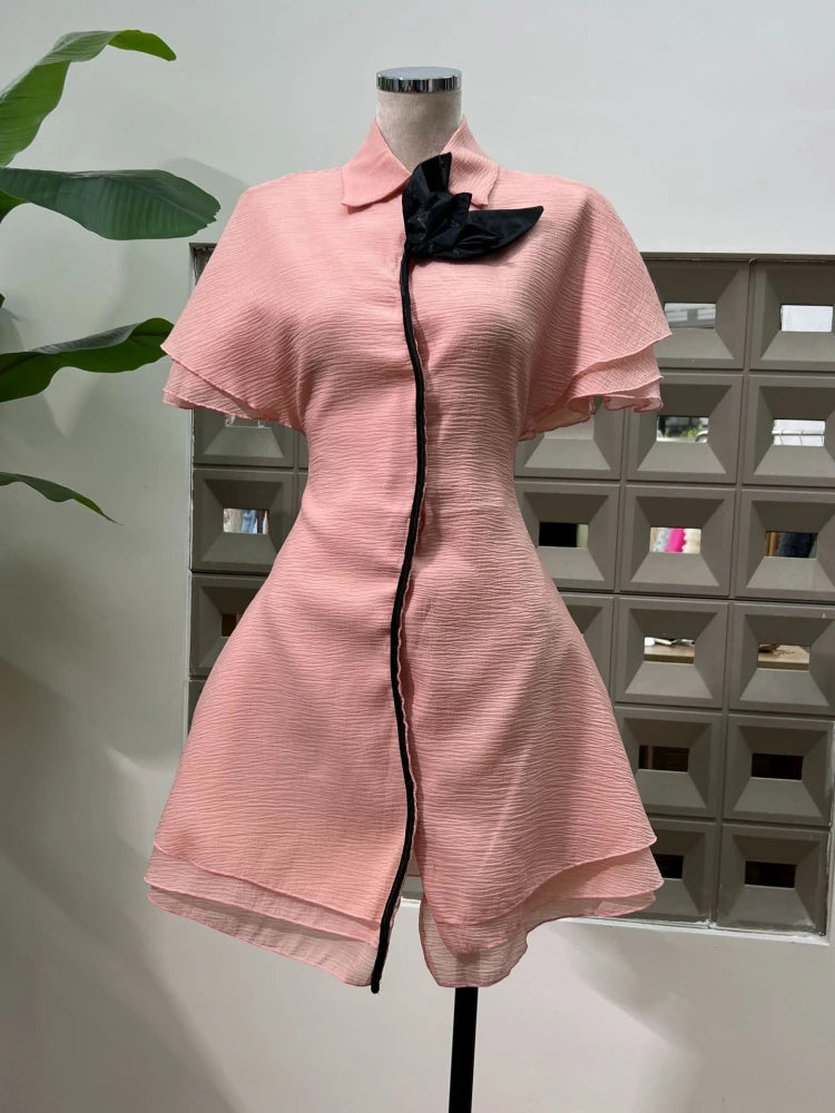 Pink dress with black trim on a mannequin against a geometric wall.