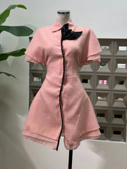 Pink dress with black trim on a mannequin against a geometric wall.