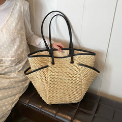 Beige woven handbag with black handles on a black leather bench.