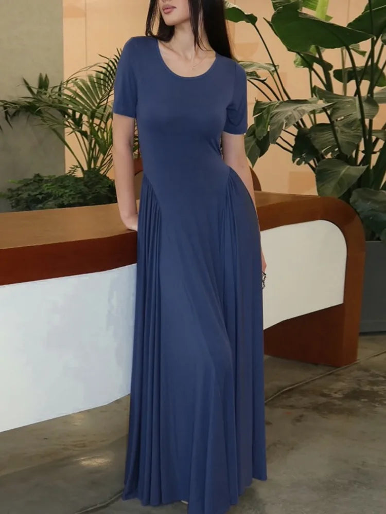 Woman wearing a blue dress standing in an indoor setting with plants.