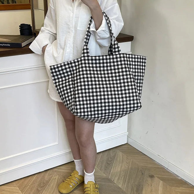 Person holding a black and white checkered bag in a room with wooden flooring.
