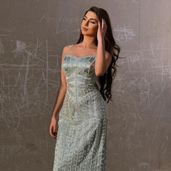 Woman in an elegant dress standing against a textured wall.