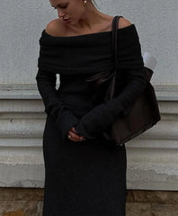 Person wearing a black off-shoulder top and skirt against a neutral wall.