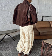 Person wearing a brown jacket and white pants standing in a room with a couch and table.