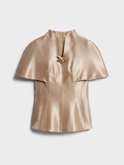 Gold metallic top with a decorative brooch on a light gray background