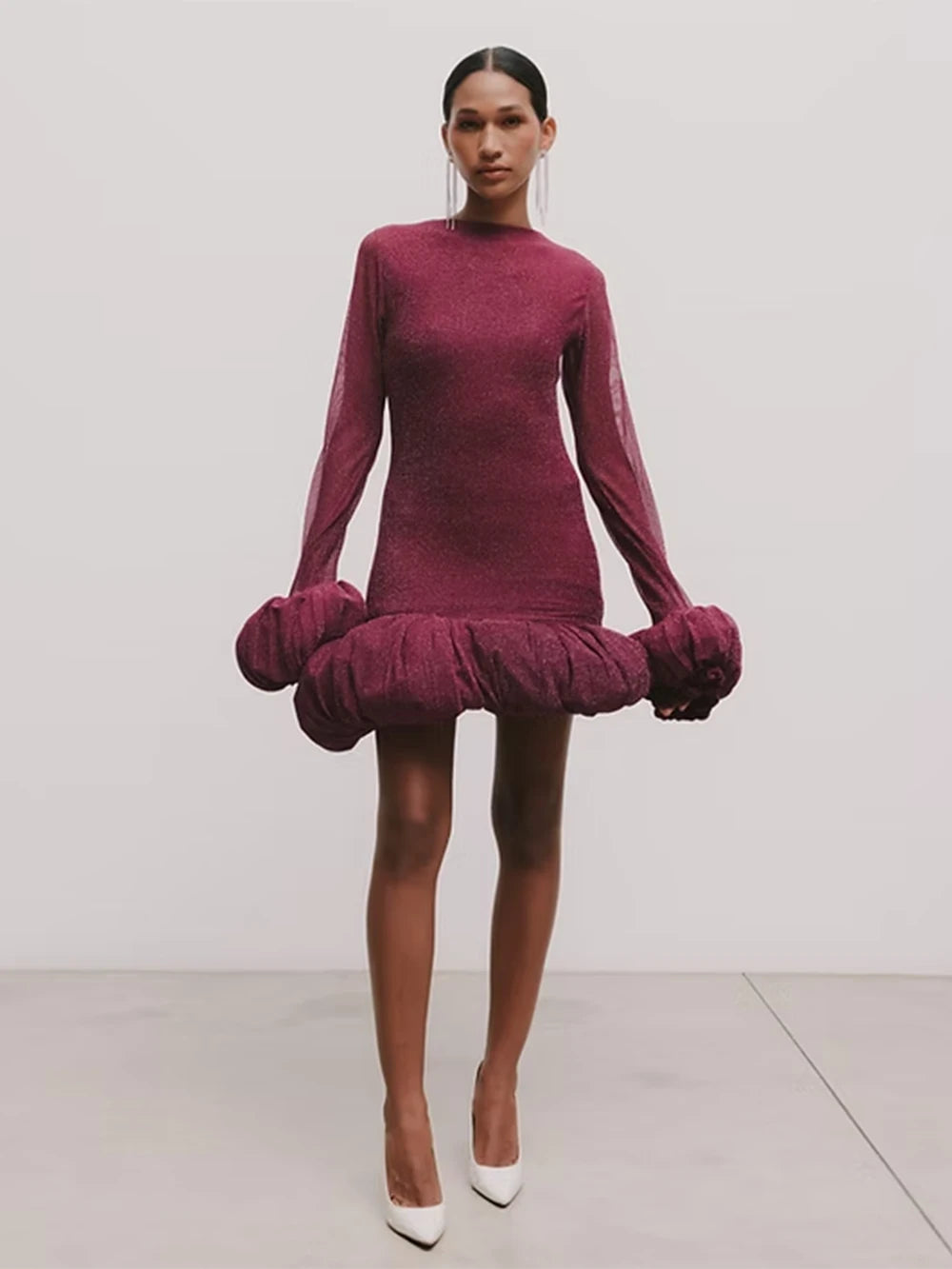 Woman wearing a burgundy dress with ruffled sleeves and hem on a plain background