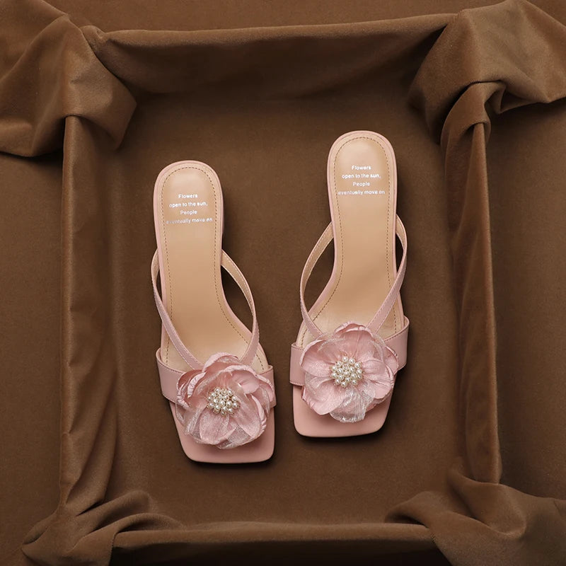 Pink high-heeled sandals with floral decorations on a brown fabric background