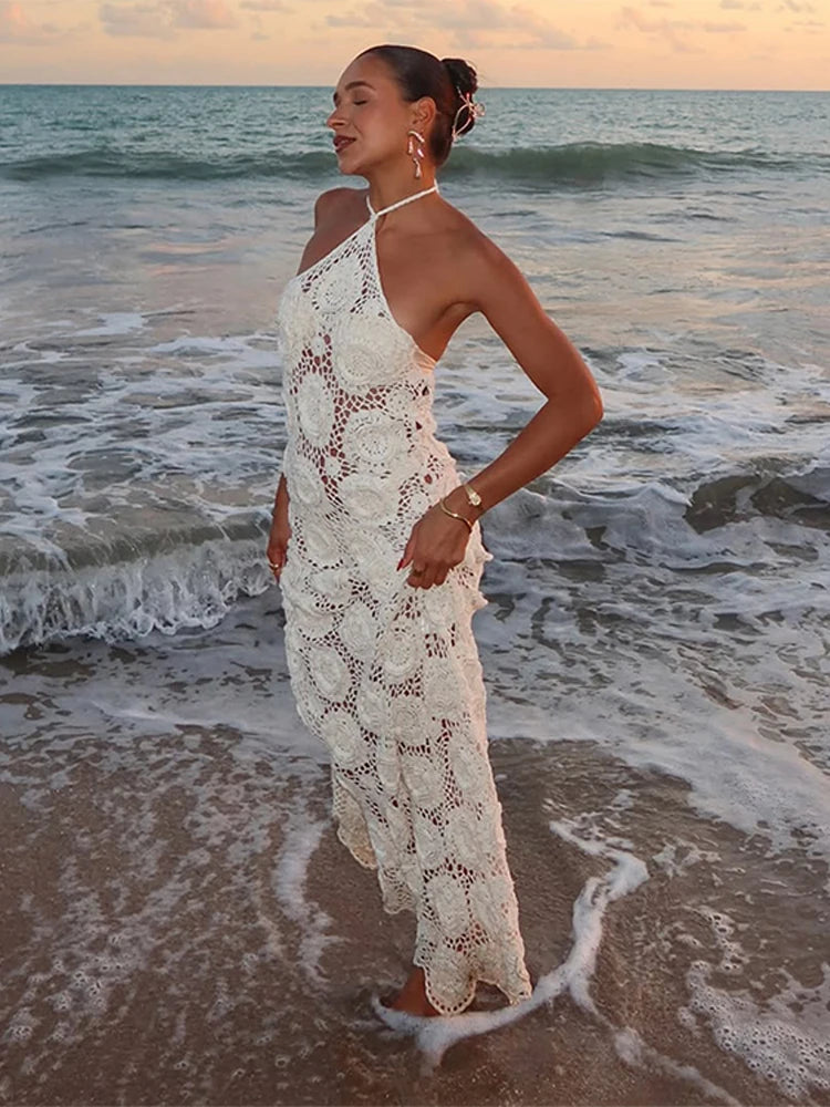 Woman in a white lace dress standing on a beach with ocean waves.