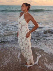 Woman in a white lace dress standing on a beach with ocean waves.