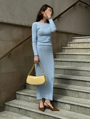 Woman in a light blue outfit standing on stairs holding a yellow handbag.