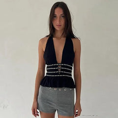 Woman wearing a black halter top with pearl details and gray shorts against a plain background
