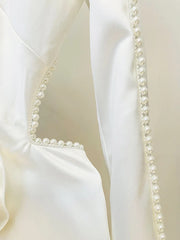 Close-up of a white garment with pearl detailing on a beige background