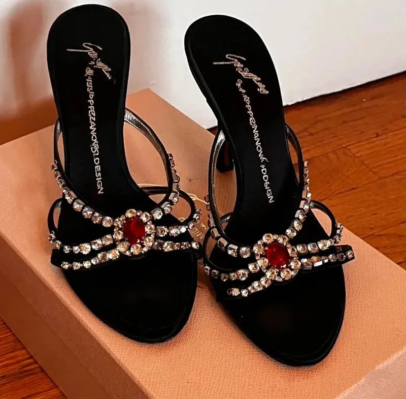 Top view of black open-toe stiletto heels with red spider gem embellishments.