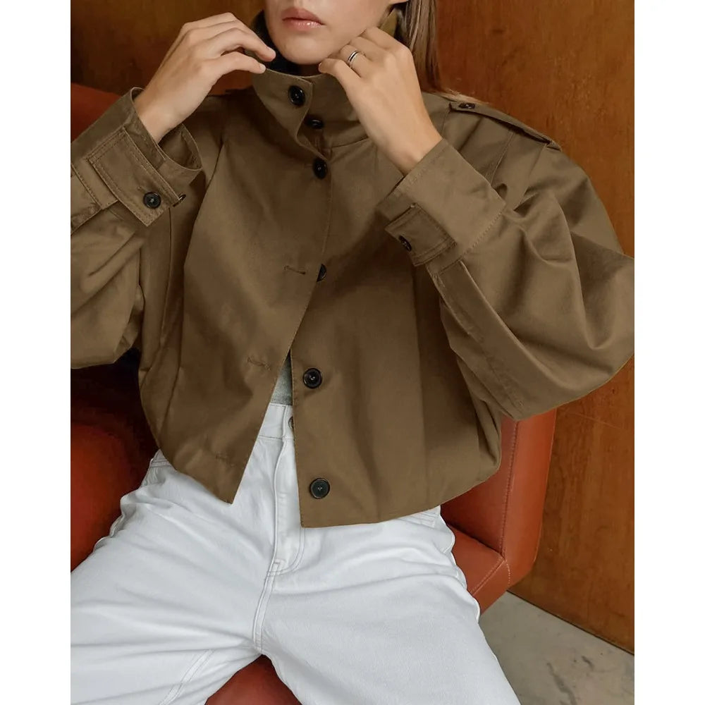 Person wearing a brown jacket and white pants sitting on an orange chair.