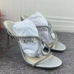 Silver high-heeled sandals with rhinestone embellishments on a carpeted floor.