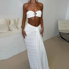 Woman wearing a white strapless top and long skirt in a minimalistic room.