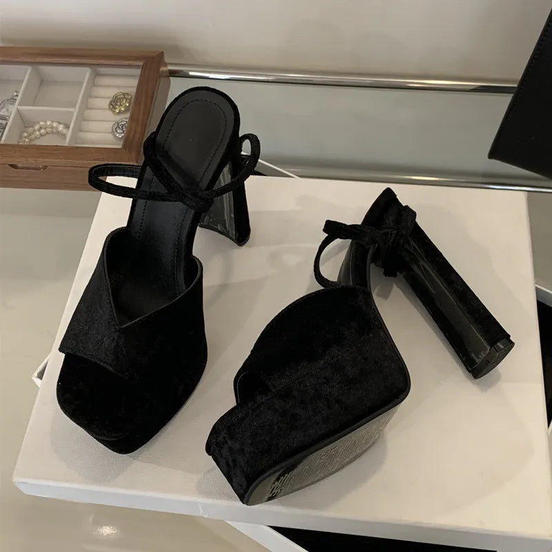 Black high-heeled shoes on a white surface with a jewelry box in the background.