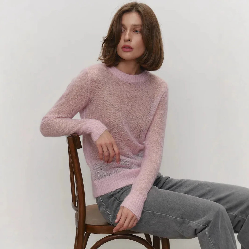 Woman wearing a pink sweater sitting on a wooden chair against a white background