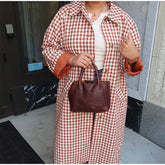 Person wearing a red and white checkered coat holding a brown handbag.