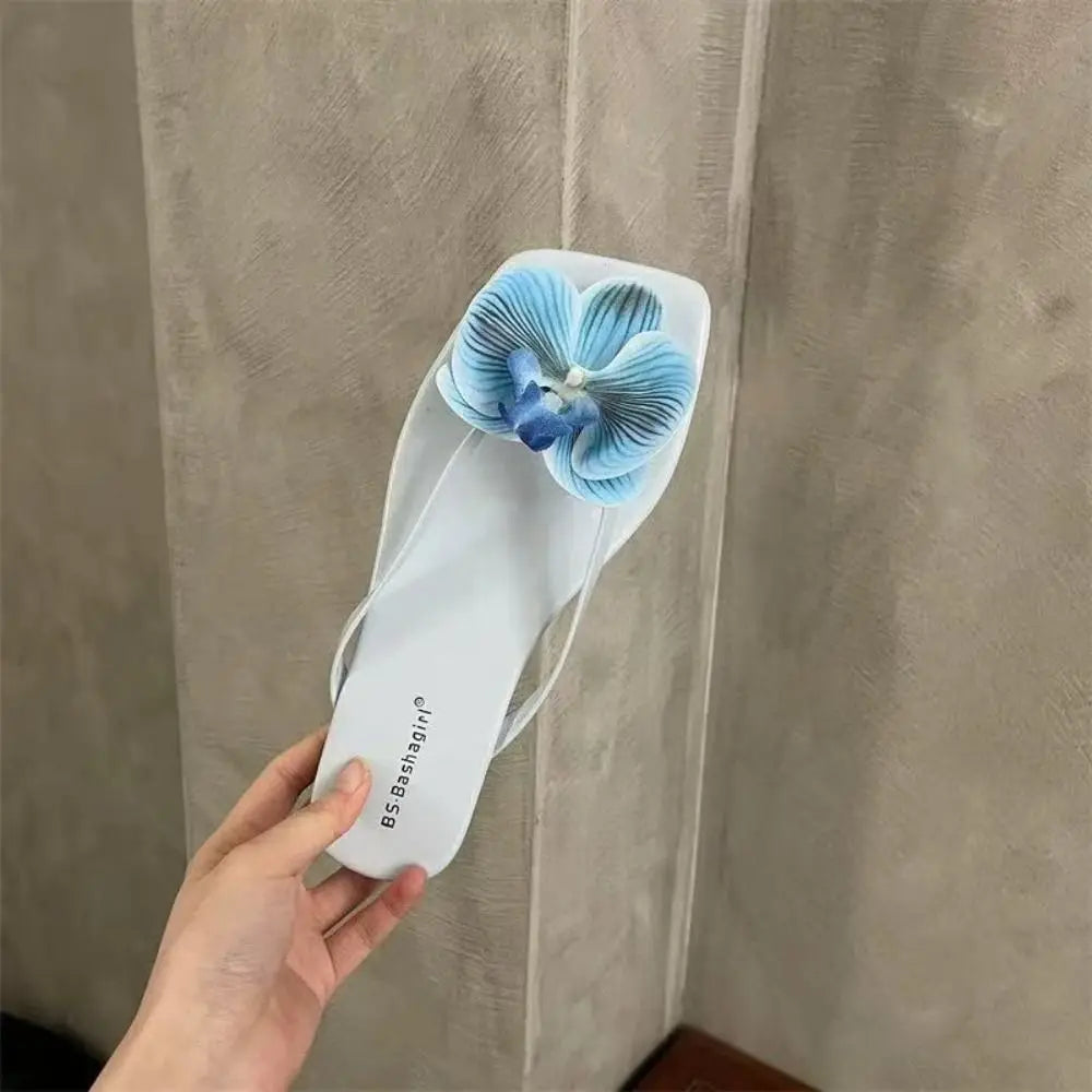 White sandal with blue flower design held against a neutral background