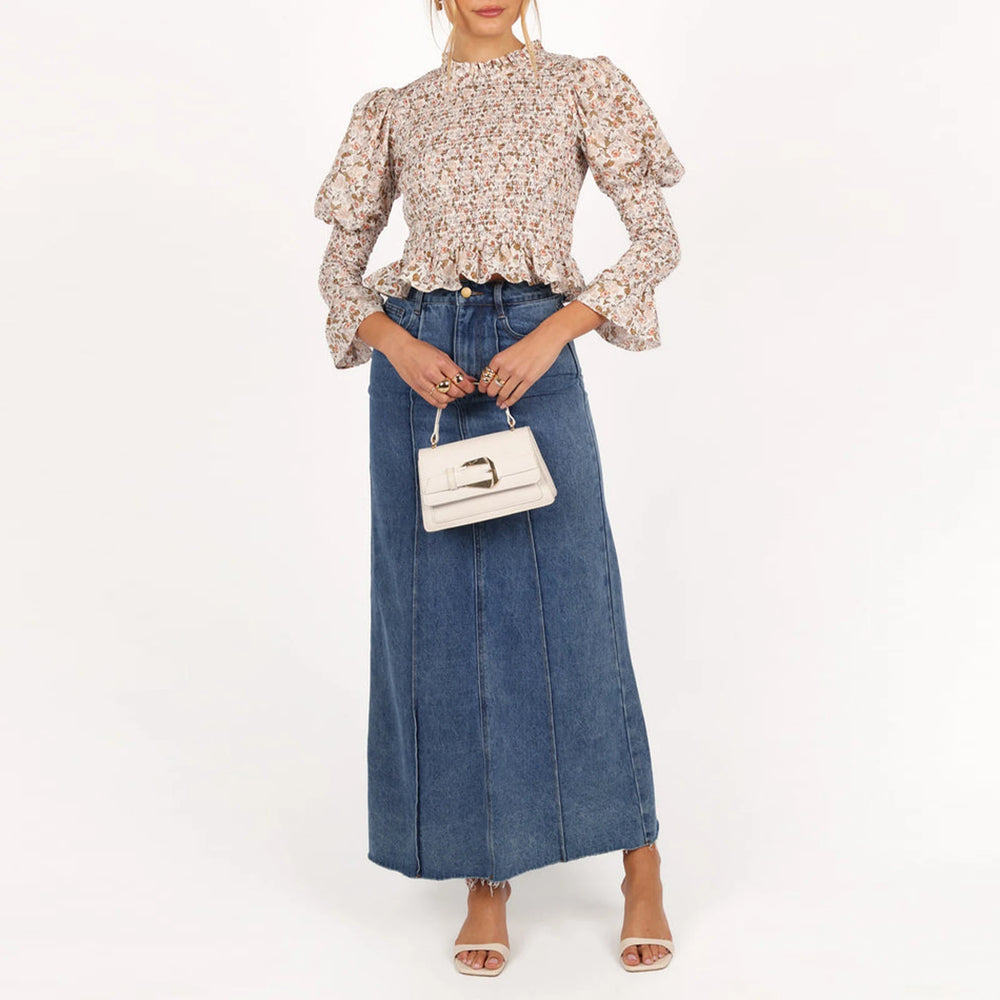 Woman wearing a floral blouse and denim skirt with a white handbag on a white background