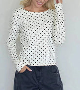 Woman wearing a white long-sleeve top with black polka dots against a light gray background