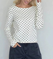 Woman wearing a white long-sleeve top with black polka dots against a light gray background