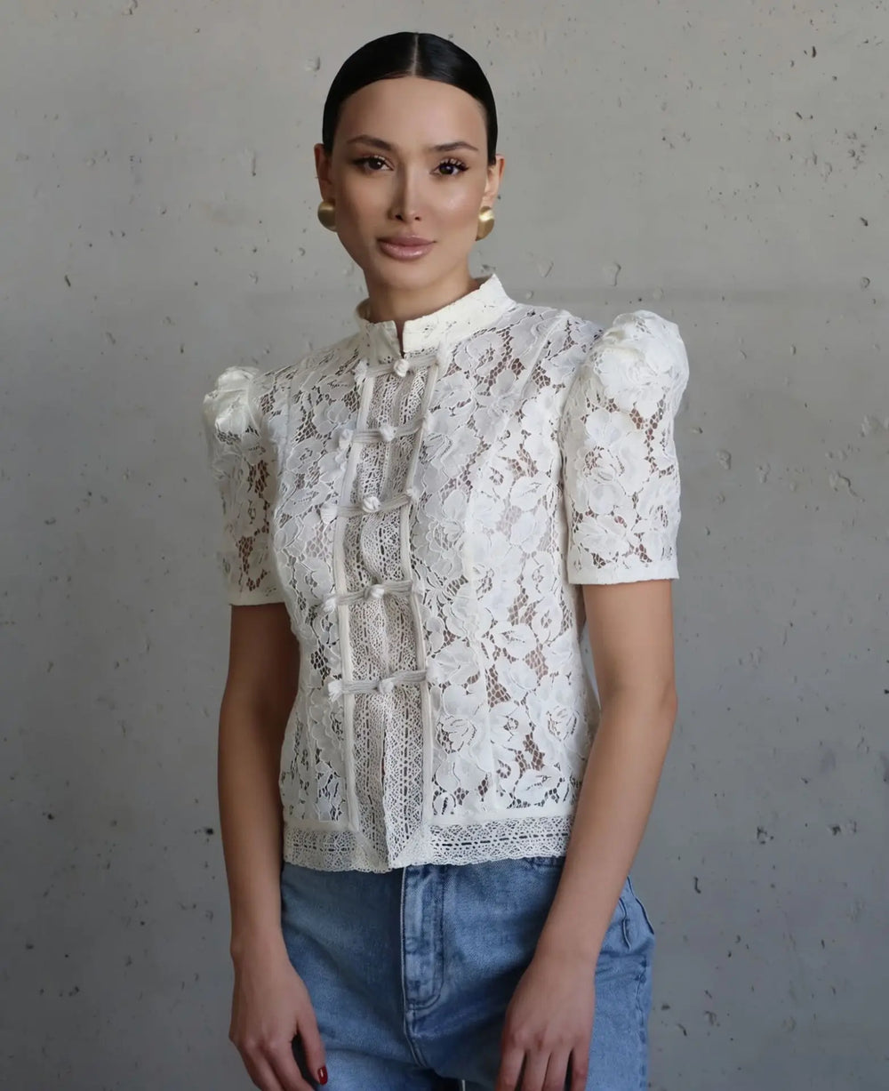 Woman wearing a white lace blouse and blue jeans against a gray background