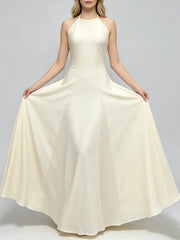Woman holding the hem of a cream halter neck a-line maxi dress with pleats.