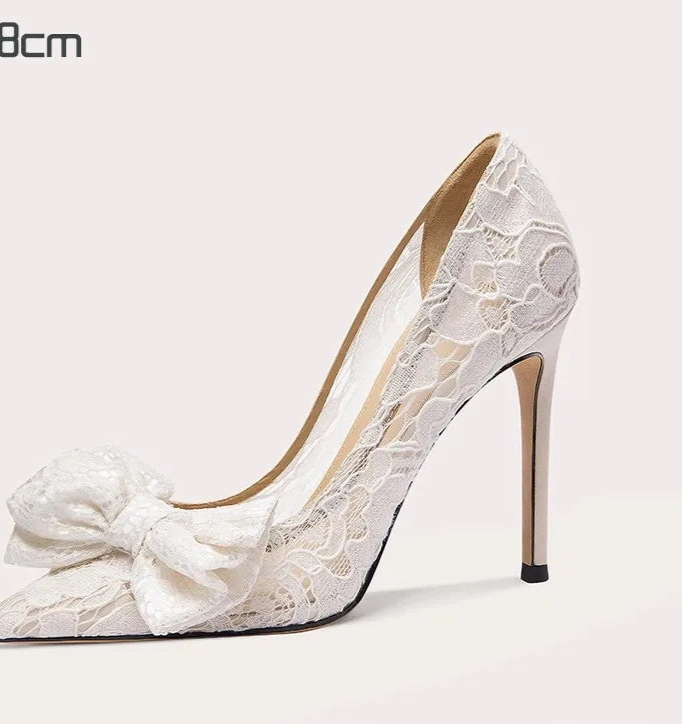 White lace high-heeled shoe with a bow on a light gray background