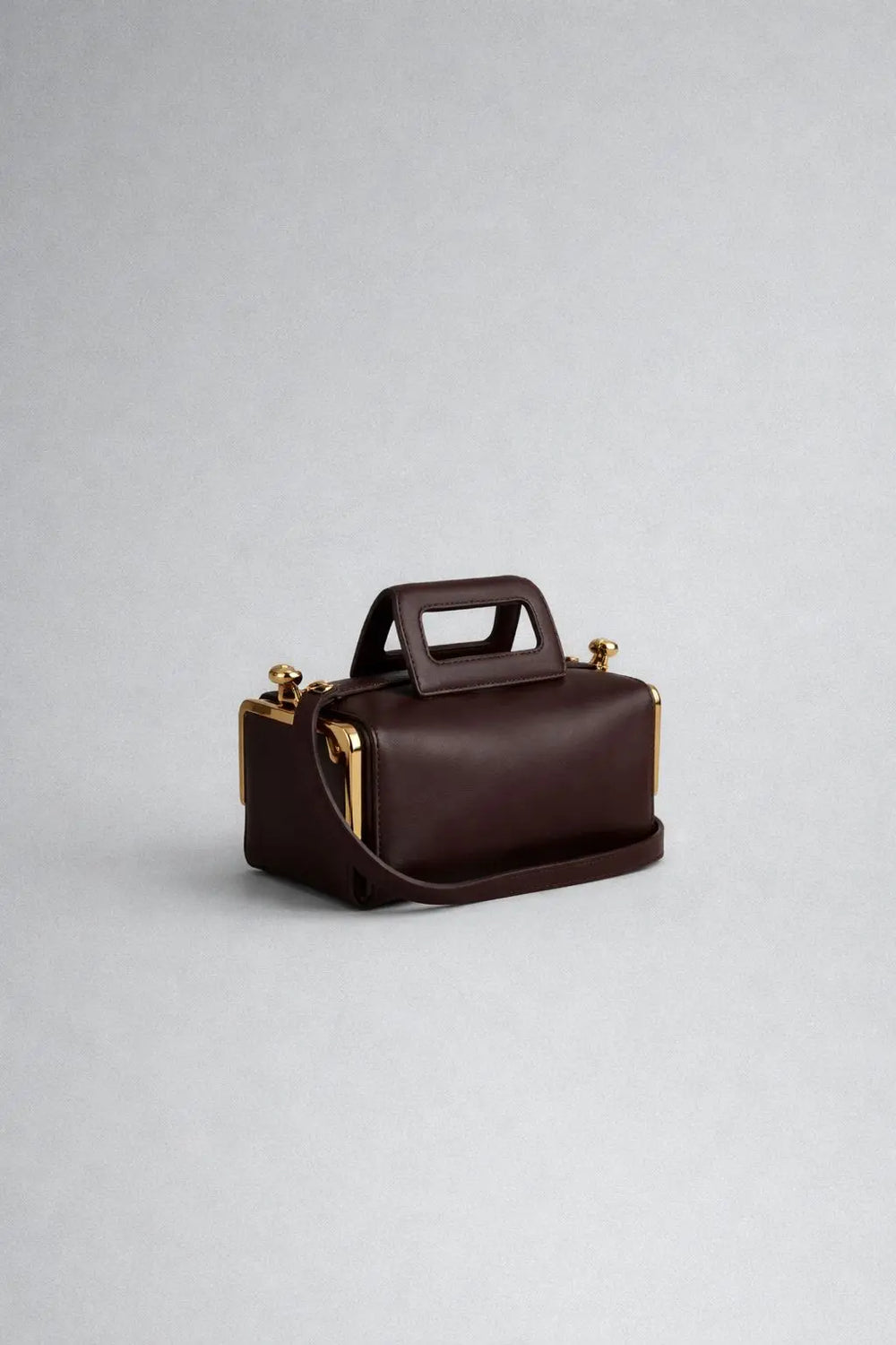 Brown leather handbag with gold accents on a light gray background