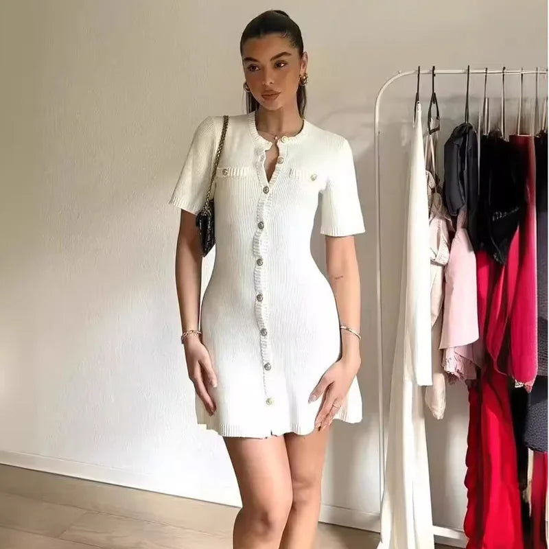 Woman wearing a white dress standing next to a clothing rack with various garments.
