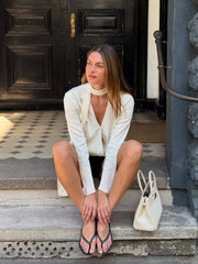 Woman sitting on steps wearing a white outfit with a black door in the background