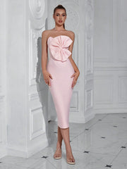 Woman wearing a pink strapless dress with a large bow in a white room.