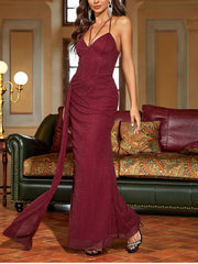 Woman in a burgundy evening gown standing in an elegant room with a green sofa and decorative pillows.