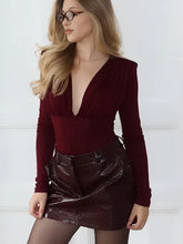 Woman wearing a burgundy bodysuit and black patent leather skirt against a white background